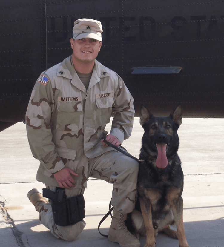 Ryan in U.S. Army uniform kneeling with his military working dog, a German Shepherd, in front of a helicopter