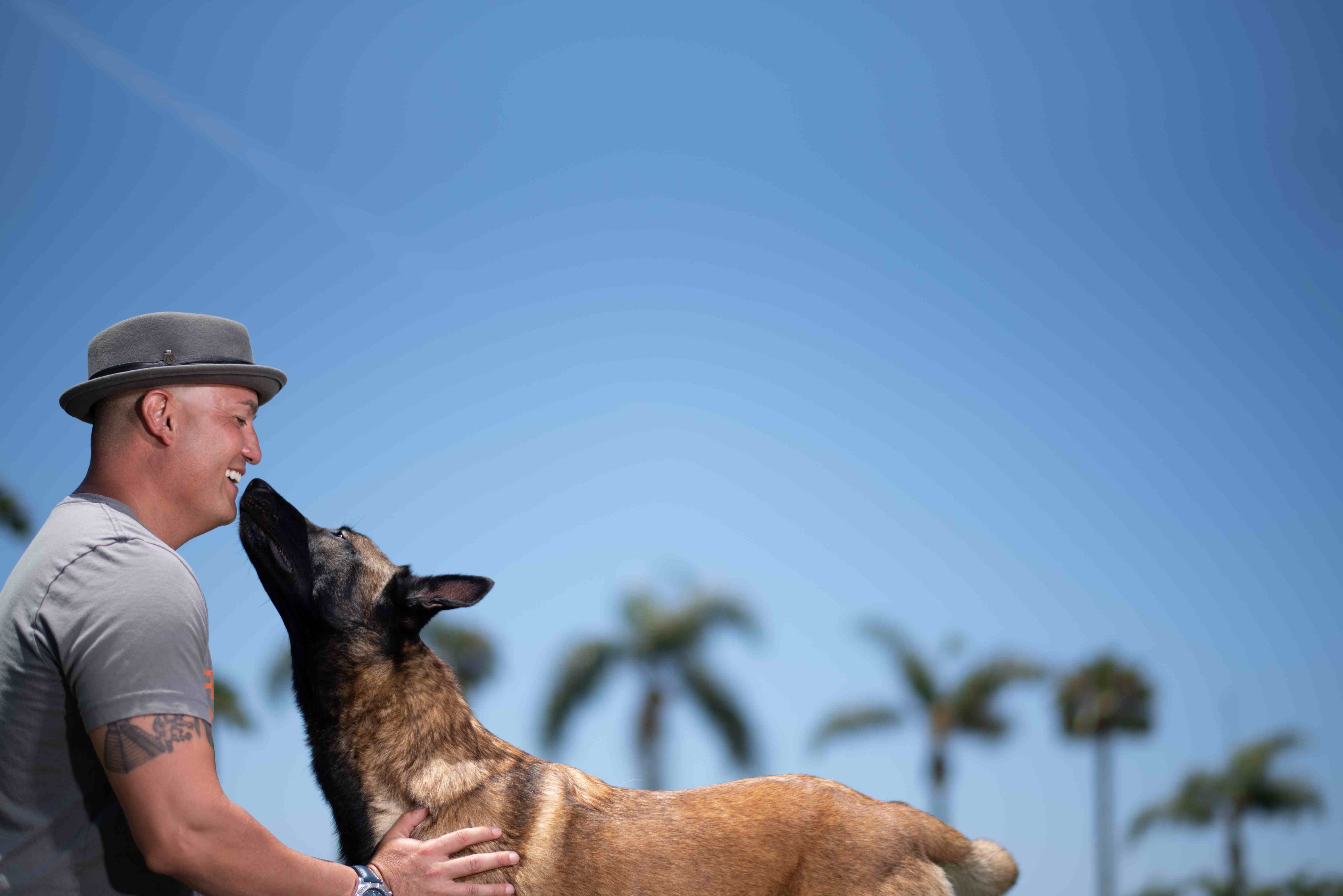 Ryan Matthews, veteran dog trainer, sharing a joyful moment nose-to-nose with a Belgian Malinois under Orange County palm trees